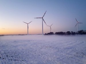 Windpark mit vier Windkraftanlagen bei Morgendämmerung im Winter. Zu sehen ist Schnee und Nebel.